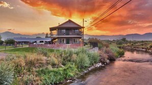 A two-story building with a balcony, surrounded by a grassy area and a stream. - Walker River Lodge (Bridgeport)