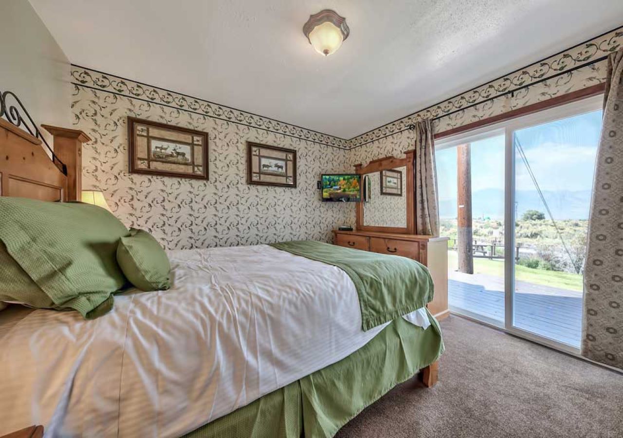 A bedroom with a bed, a dresser, a TV, and a large window with a view.