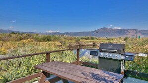 A wooden deck with a grill and a picnic table overlooking a natural landscape with mountains in the distance. - Walker River Lodge (Bridgeport)