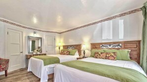 Une chambre d’hôtel avec deux lits, des têtes de lit en bois, une literie verte, un miroir, une table de chevet et une chaise.