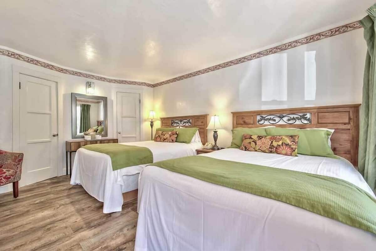 Une chambre d’hôtel avec deux lits, des têtes de lit en bois, une literie verte, un miroir, une table de chevet et une chaise.