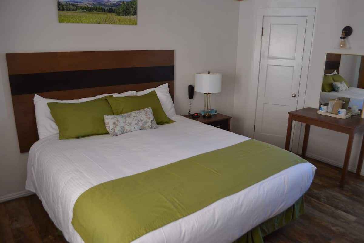 Un lit bien fait, recouvert d’une couvre-lit verte et blanche, avec une tête de lit en bois et une table de chevet sur laquelle se trouvent une lampe et un téléphone.