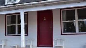 A single-story building with a red door, white exterior walls, and a small porch with two white chairs.