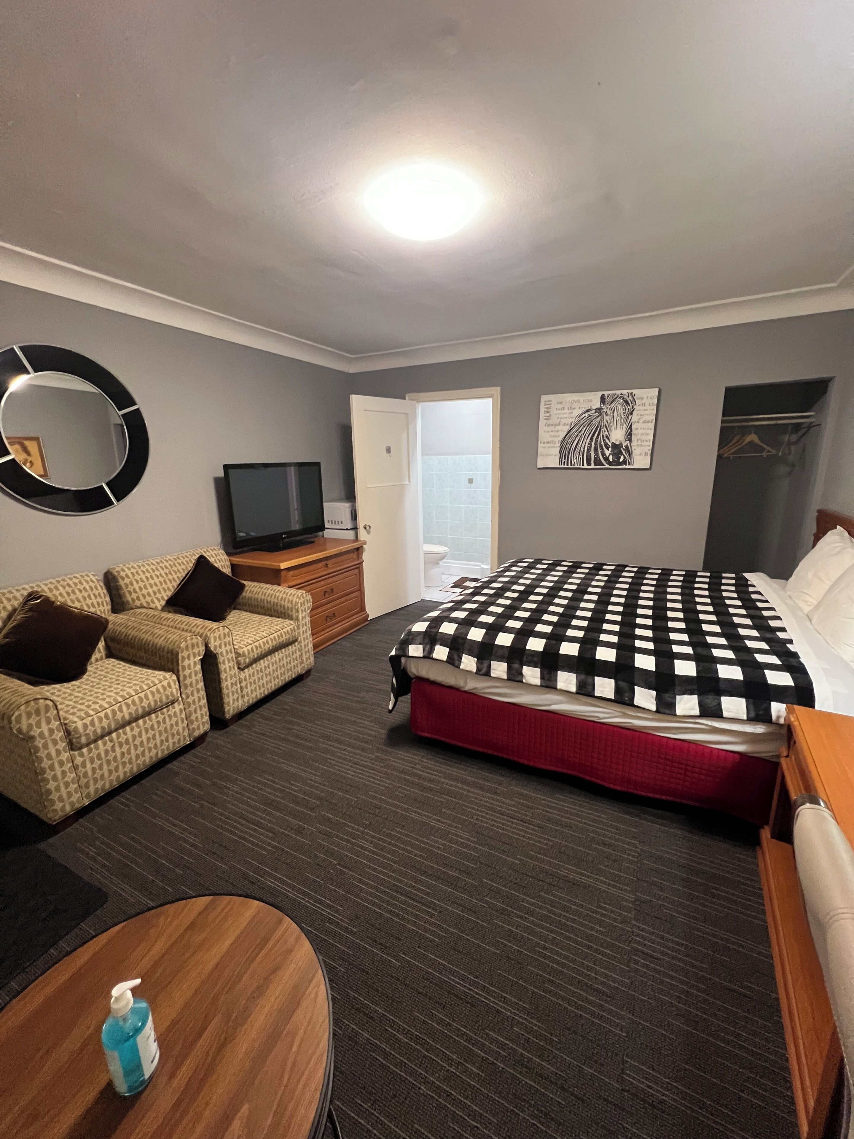 A hotel room with a bed, two sofas, a TV, a mirror, and a bathroom door.