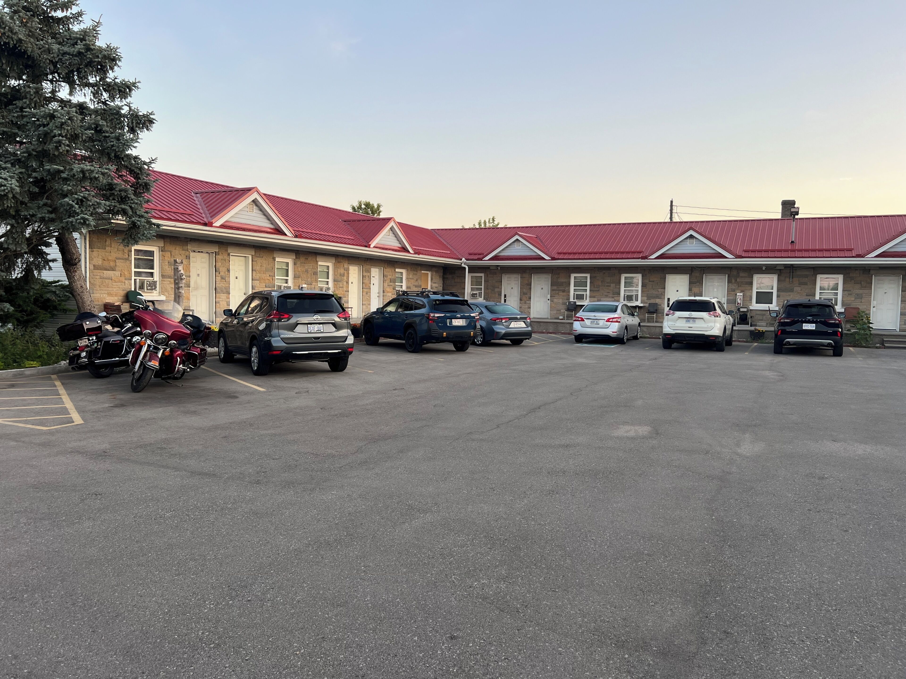 A motel with a red roof, parked cars, and motorcycles in the parking lot.
