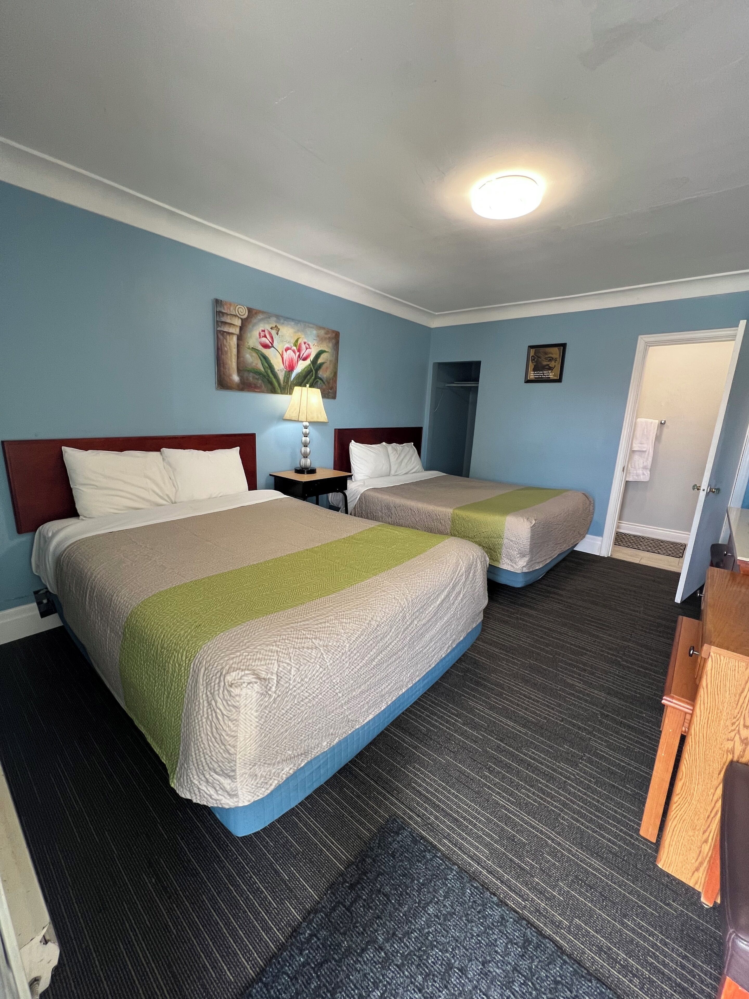 A hotel room with two beds, a nightstand, a lamp, a painting, and a door.