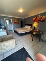 Habitación de hotel con cama, escritorio, silla, lámpara y obras de arte en la pared.