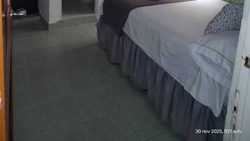Un dormitorio con una cama, un televisor montado en la pared, una ventana con cortinas y una puerta que da al baño.