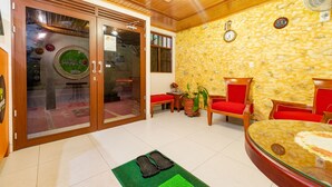 Un vestíbulo de hotel con pared de piedra, sillas rojas, un reloj y una mesa de vidrio.