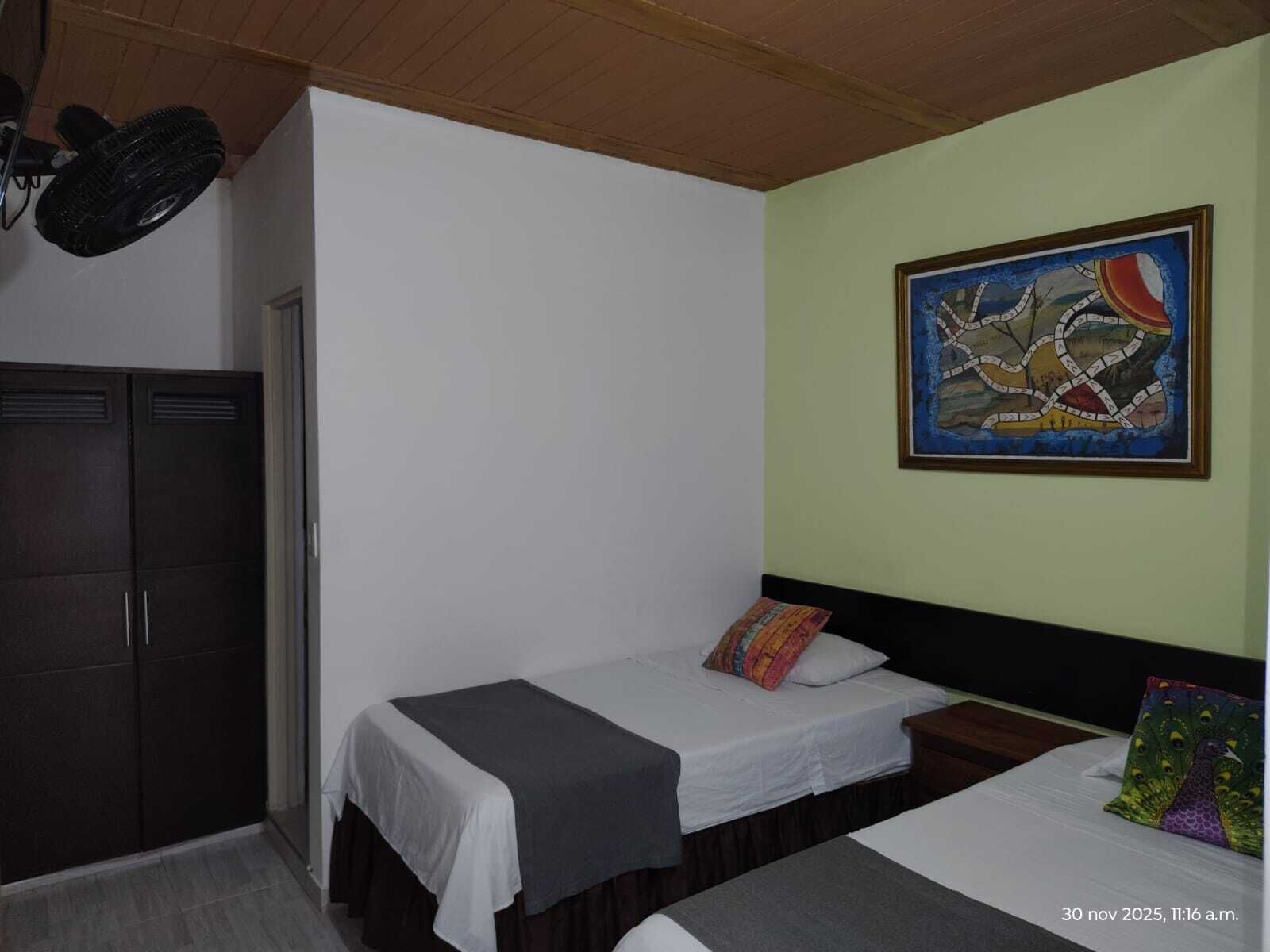 A room with two single beds, a wardrobe, and a ceiling fan.