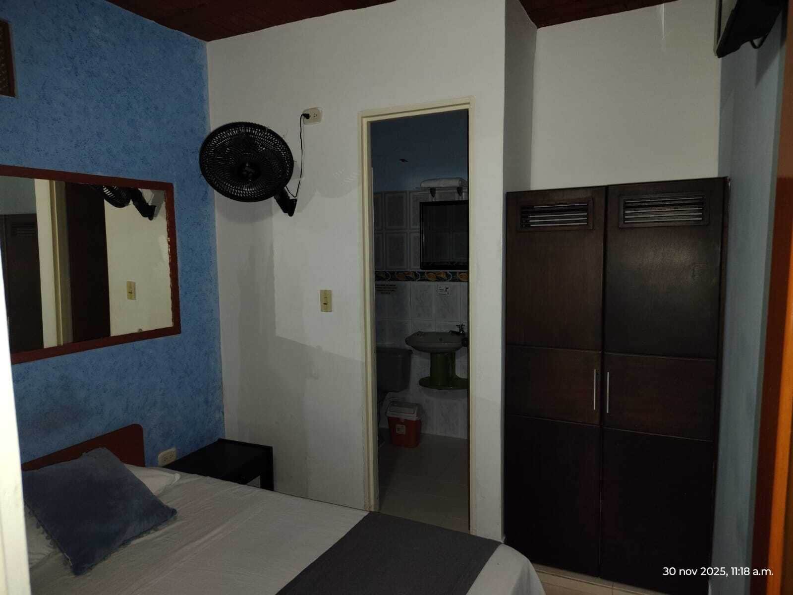 Una camera da letto con un letto, un comodino, uno specchio, una ventola e un armadio.