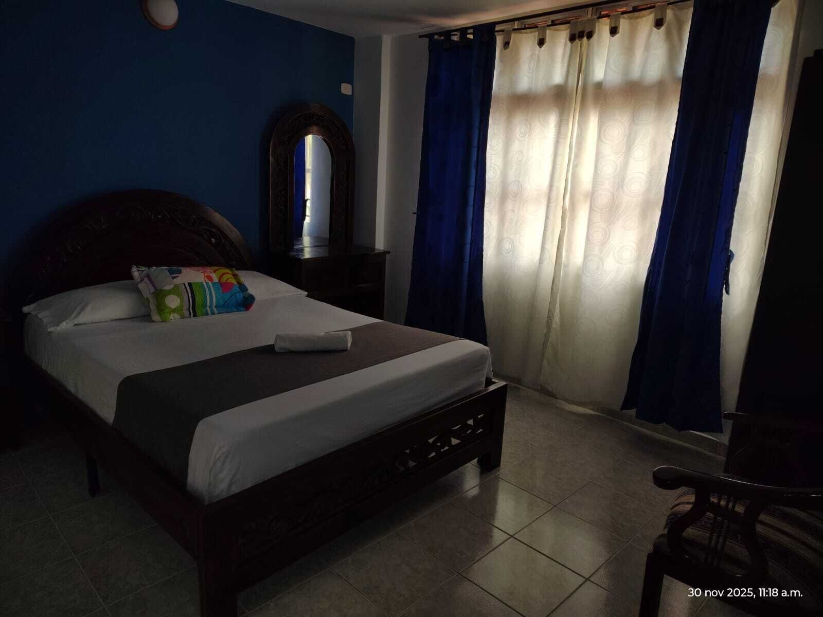 A bedroom with a bed, a nightstand, a mirror, and a chair.