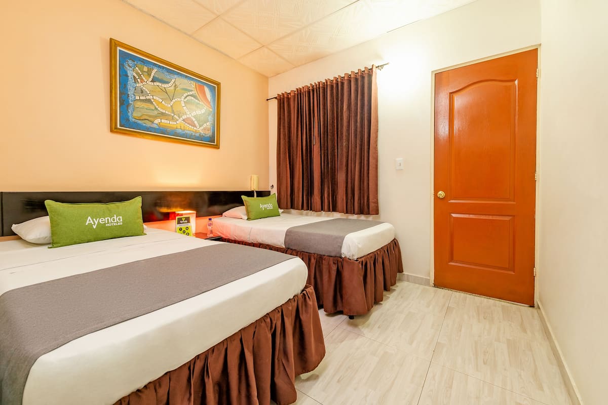 Ein Hotelzimmer mit zwei Betten, einem Gemälde an der Wand, einer Tür und einem Nachttisch mit Lampe.