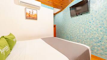 Une chambre d’hôtel avec un lit, un téléviseur fixé au mur, un appareil de climatisation et un papier peint à motifs floraux.