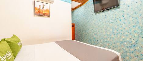 Habitación de hotel con cama, televisión montada en la pared, aire acondicionado y papel tapiz con estampado floral.