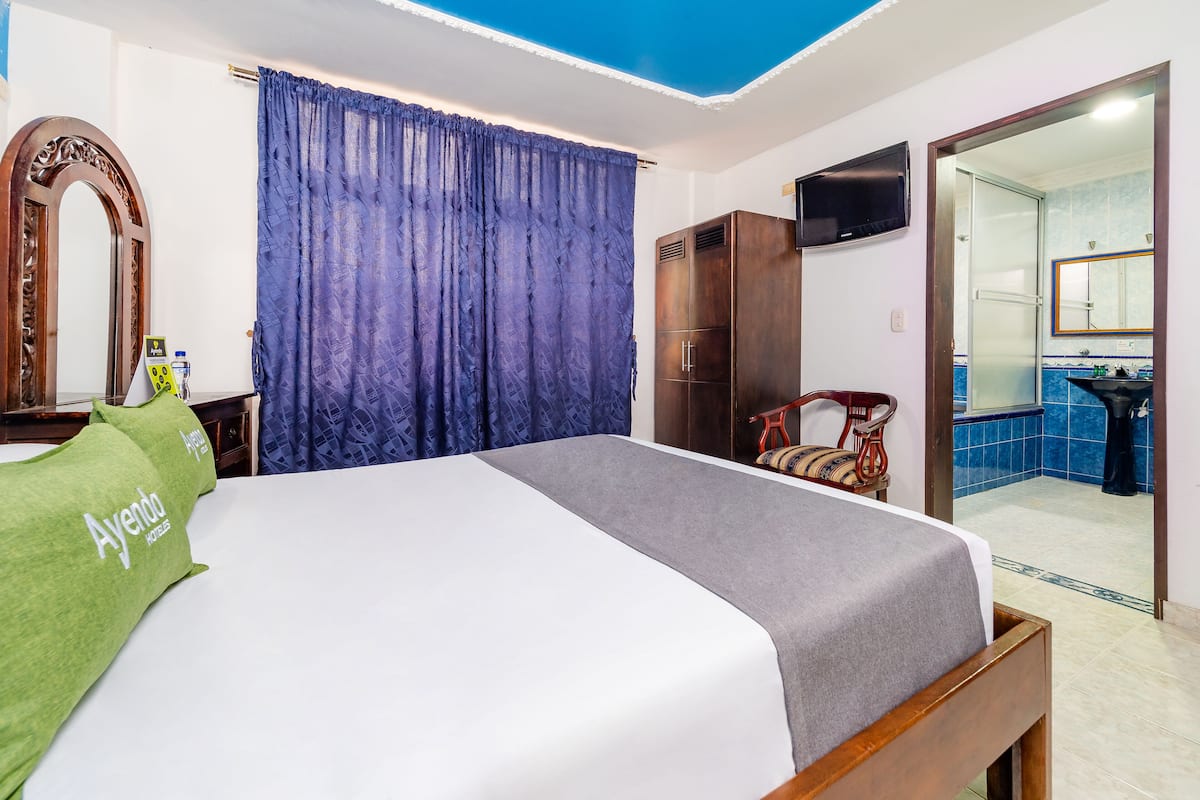 Ein Hotelzimmer mit Bett, Schrank, Fernseher und einem durch eine offene Tür einsehbaren Badezimmer.
