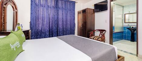 Una habitación de hotel con cama, armario, televisión y baño visible a través de una puerta abierta.