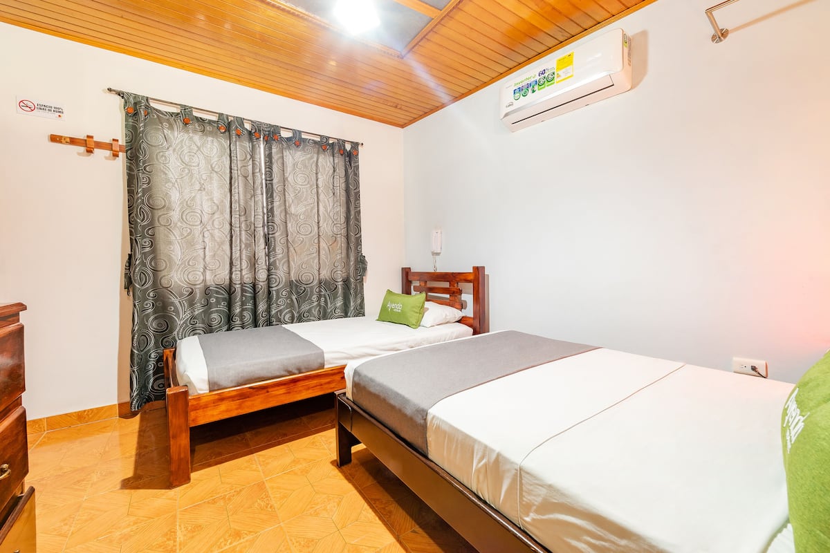 Ein Zimmer mit zwei Betten, einer Holzbalkendecke, einer Klimaanlage und einem gemusterten Vorhang.