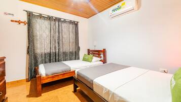 A room with two beds, a wooden ceiling, an air conditioner, and a patterned curtain.