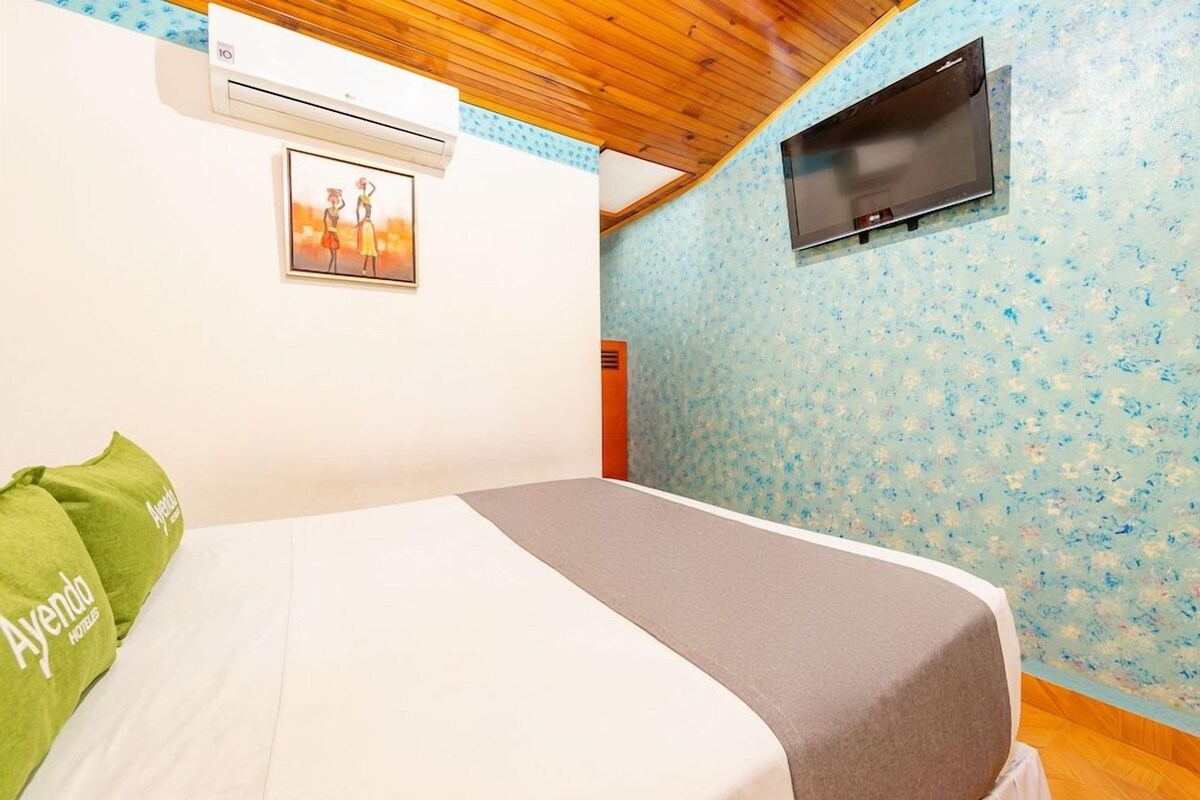 Habitación de hotel con cama, aire acondicionado, televisor montado en la pared y un marco de fotos.
