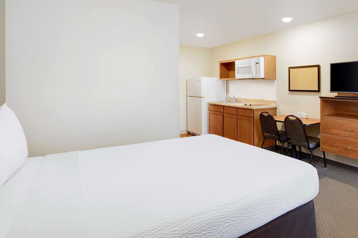A hotel room with a bed, a desk with a chair, a microwave, a refrigerator, a television, and a small cabinet.