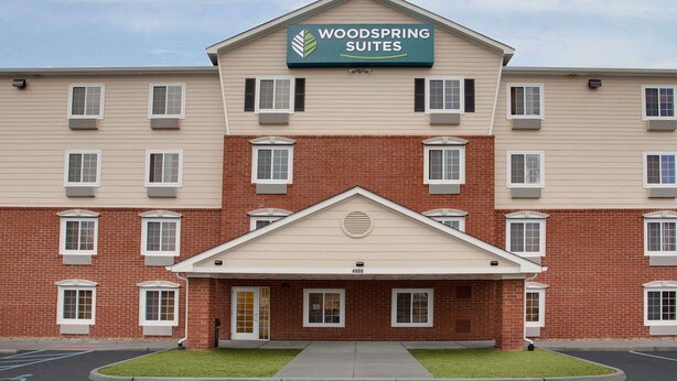 Un hotel a più piani con un cartello che recita "Woodspring Suites". Presenta una facciata in mattoni, numerose finestre e un ingresso centrale con una porta.
