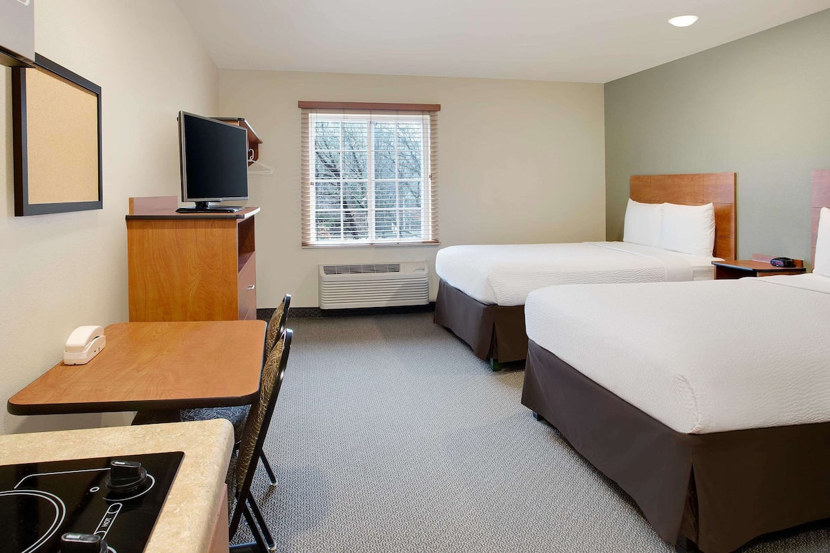 A hotel room with two beds, a desk with a telephone, a television, and a window with blinds.
