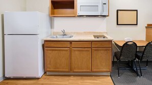 Una cucina compatta con frigorifero, forno a microonde, lavello e mobili impiallacciati.