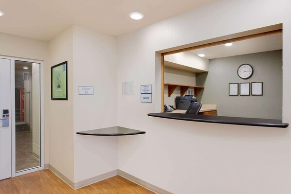 A reception area with a counter, a clock, and framed certificates on the wall. - WoodSpring Suites Virginia Beach (Virginia Beach)