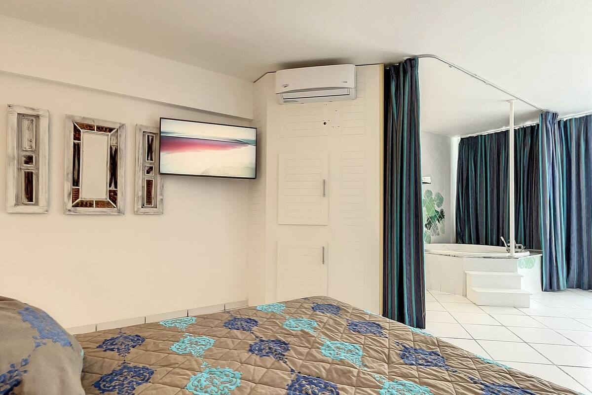A hotel room with a bed, a TV, an air conditioning unit, a bathroom with a bathtub, and a staircase.