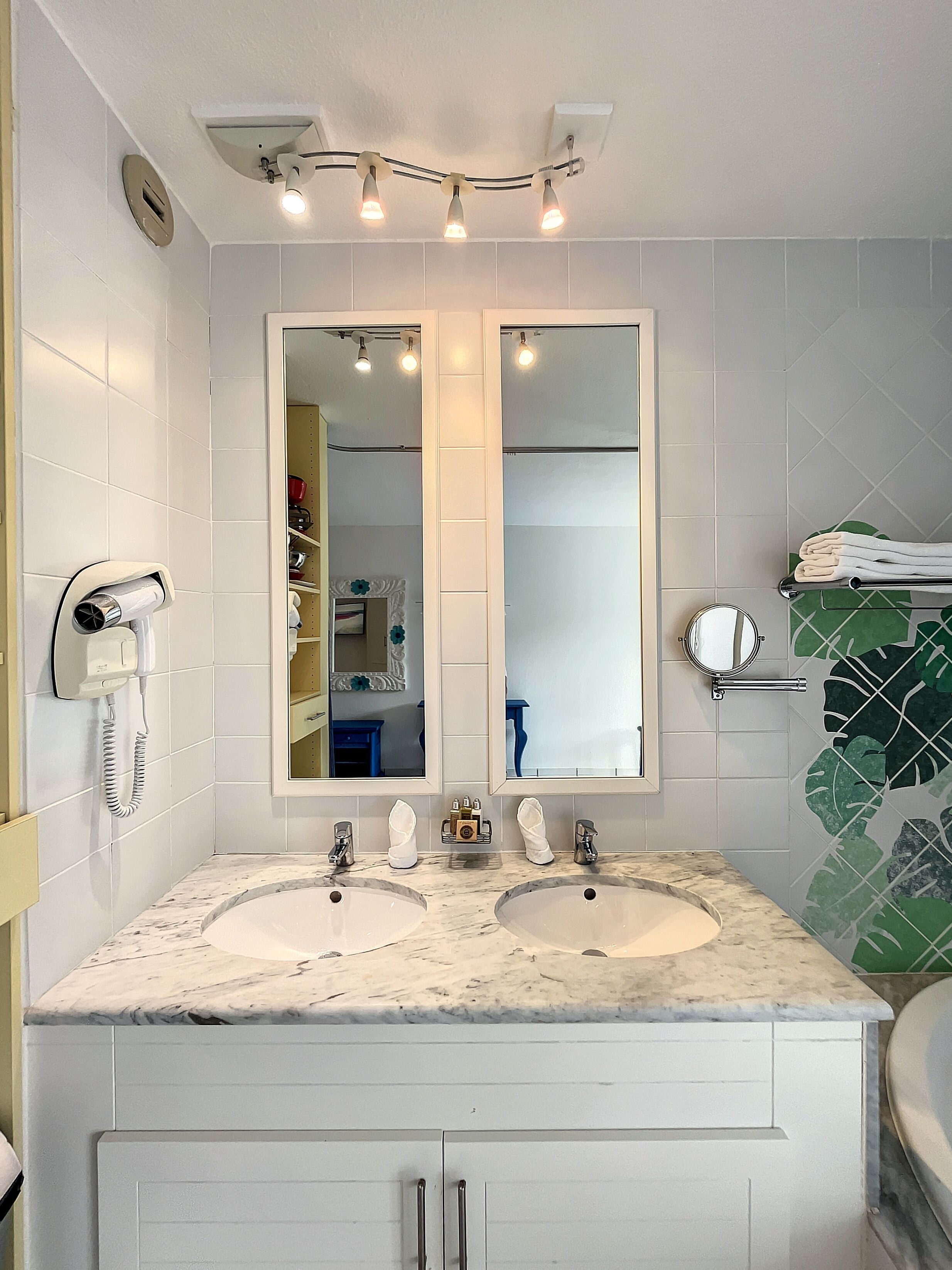 A bathroom with two sinks, a large mirror, a hairdryer, and a towel rack.