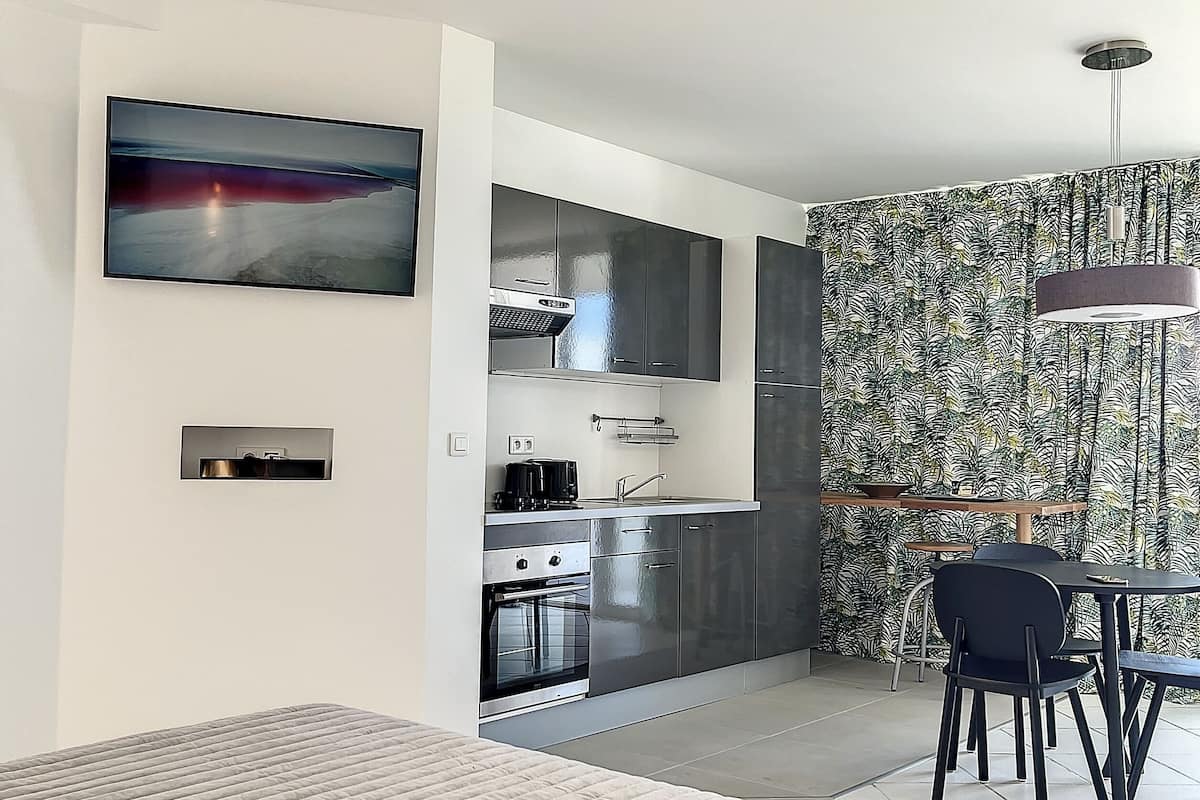 A modern kitchen with stainless steel appliances, a dining area with a table and chairs, and a large painting on the wall.