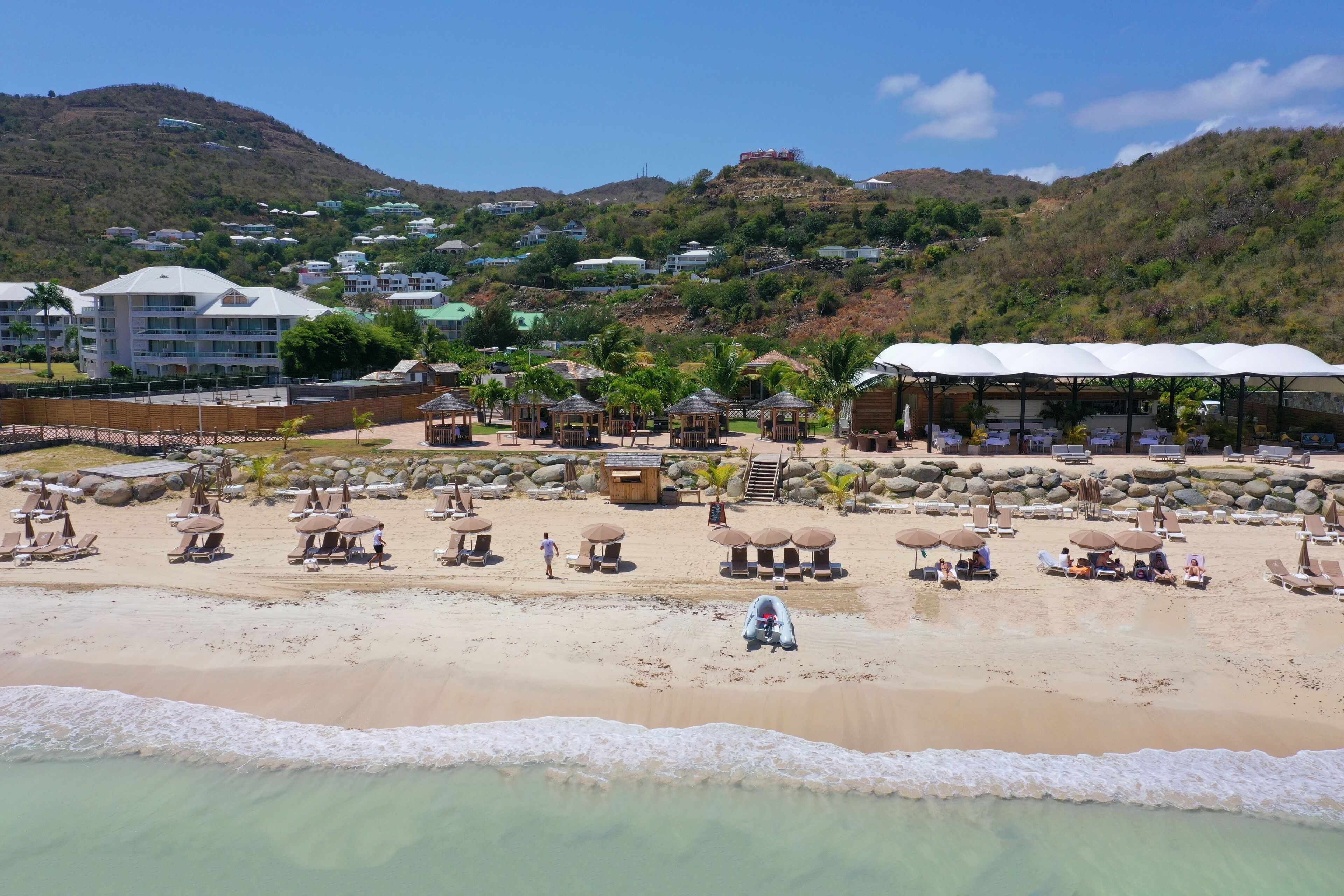 Un resort frente al mar con varias cabañas y una playa de arena, con montañas al fondo.