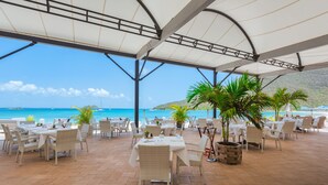 An outdoor dining area with tables and chairs, overlooking a beach and ocean. - Le Domaine Anse Marcel Beach Resort (Anse Marcel)