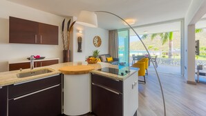 A modern kitchen with a built-in island, a dining area with yellow chairs, and a view of the outdoors. - Le Domaine Anse Marcel Beach Resort (Anse Marcel)