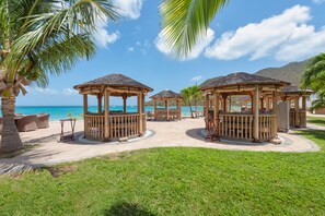 A beachside resort with wooden gazebos, lounge chairs, and a palm tree. - Le Domaine Anse Marcel Beach Resort (Anse Marcel)
