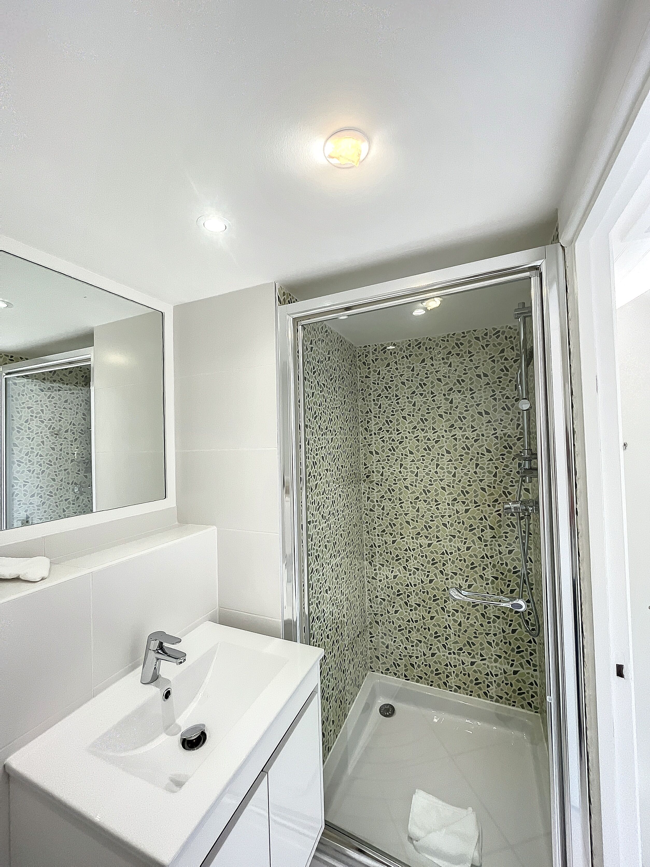 A modern bathroom with a white sink, mirror, and shower enclosure with mosaic tiles.