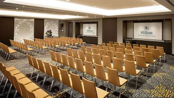 A conference room with rows of chairs, a podium, and a screen displaying the Hilton logo.