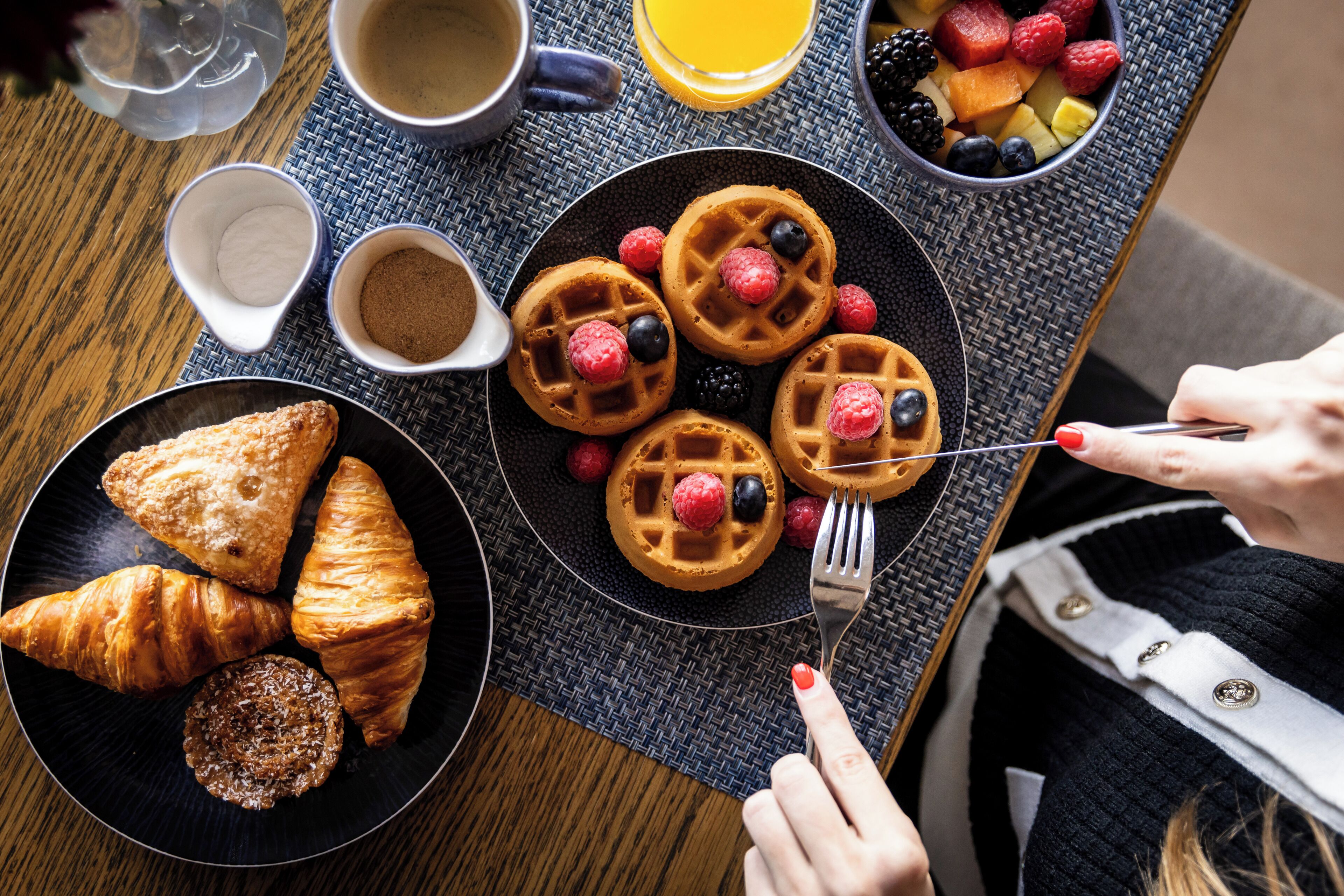 A breakfast setting with waffles, pastries, and a fruit bowl on a table.