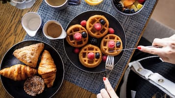 A breakfast setting with waffles, pastries, and a fruit bowl on a table.