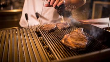 Una persona asando filetes a la parrilla, con marcas visibles de la parrilla y humo.