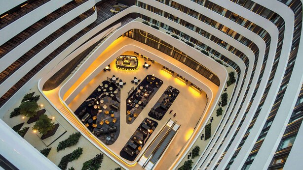 Un atrium à plusieurs niveaux, doté d’un espace central ouvert comprenant des coins salon et une longue table, le tout entouré de balcons et d’escaliers.