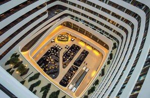 Un atrio de varios niveles con un espacio central abierto, con áreas de descanso y una mesa larga, rodeado de balcones y escaleras.