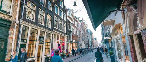 A street lined with historic buildings, some with shops and signs, and people walking and cycling.