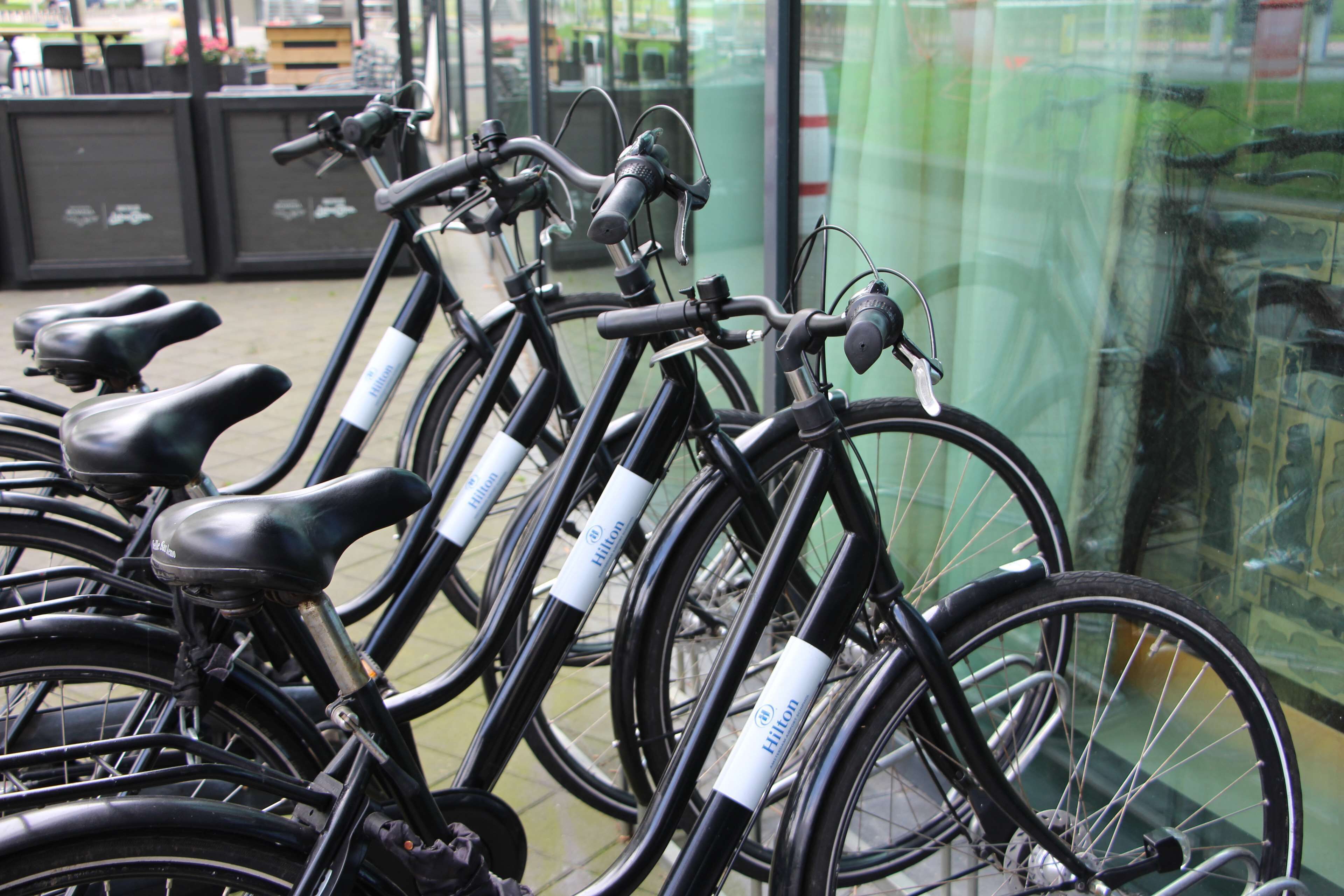 A row of bicycles with white labels, parked in front of a building with glass doors.