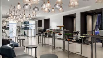 A modern hotel lobby with a long reception desk, multiple seating areas, and a variety of decorative hanging lights.