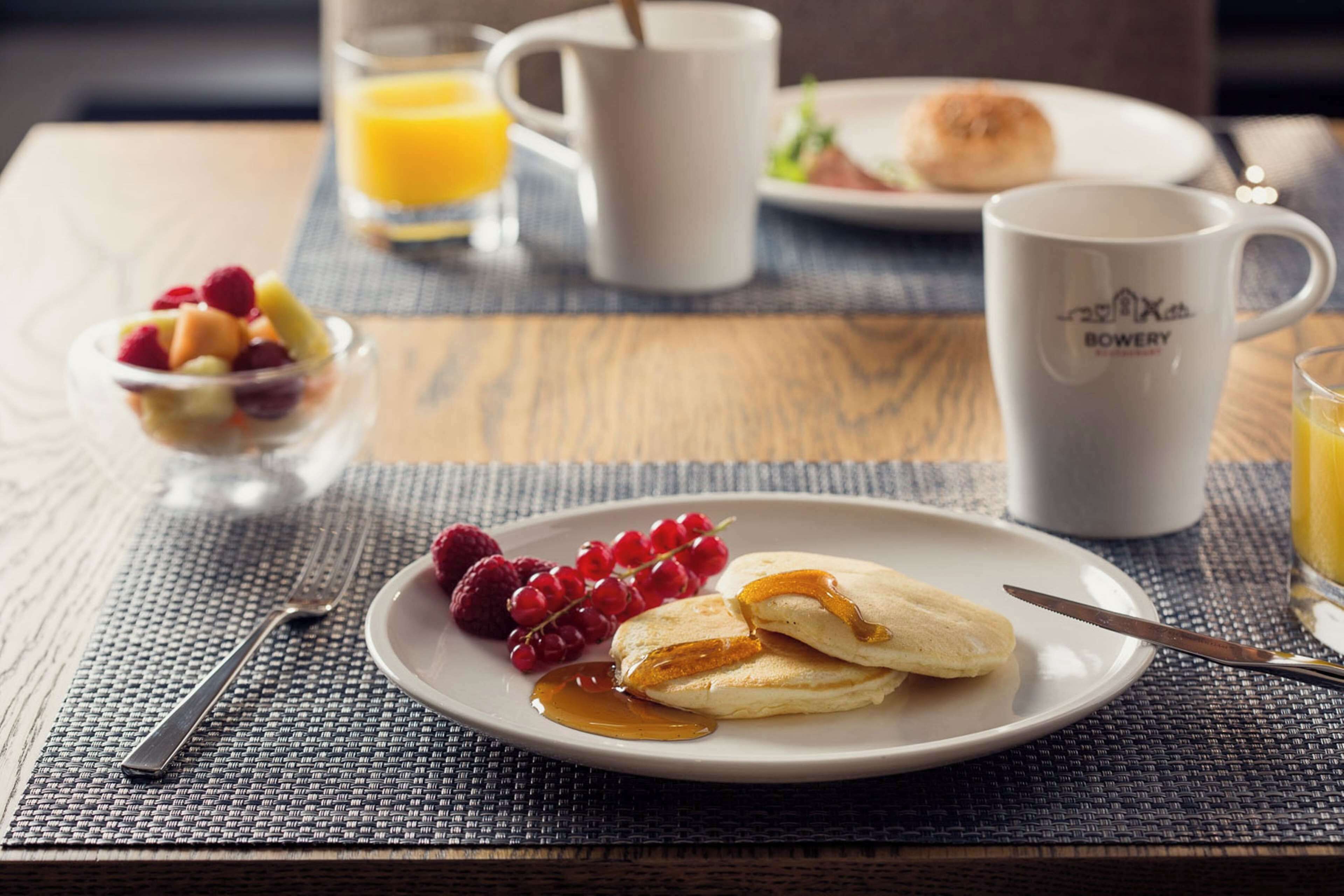 A breakfast setting with pancakes, berries, and a mug on a table.