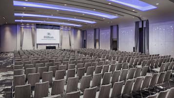 A large, modern conference room with rows of chairs, a stage with a Hilton sign, and a star-patterned wall.