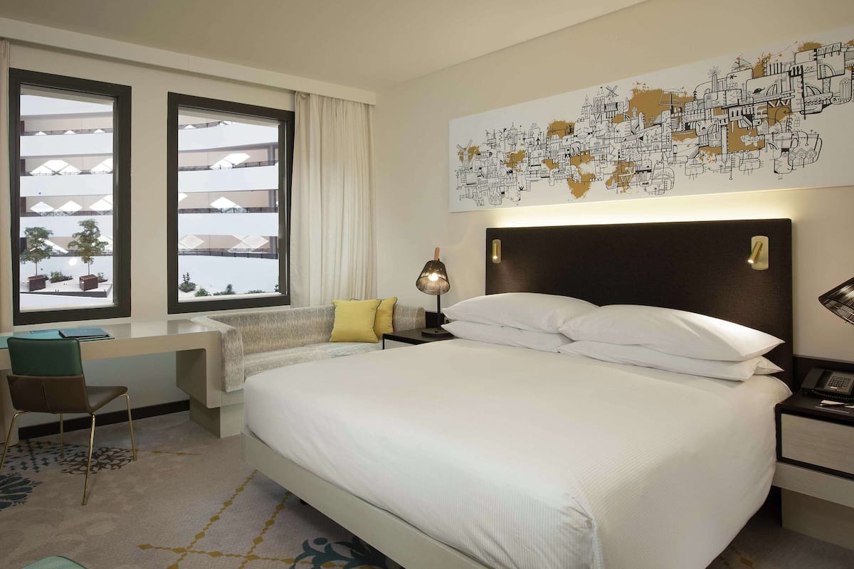 Una habitación de hotel con cama, escritorio, silla y un ventanal grande.