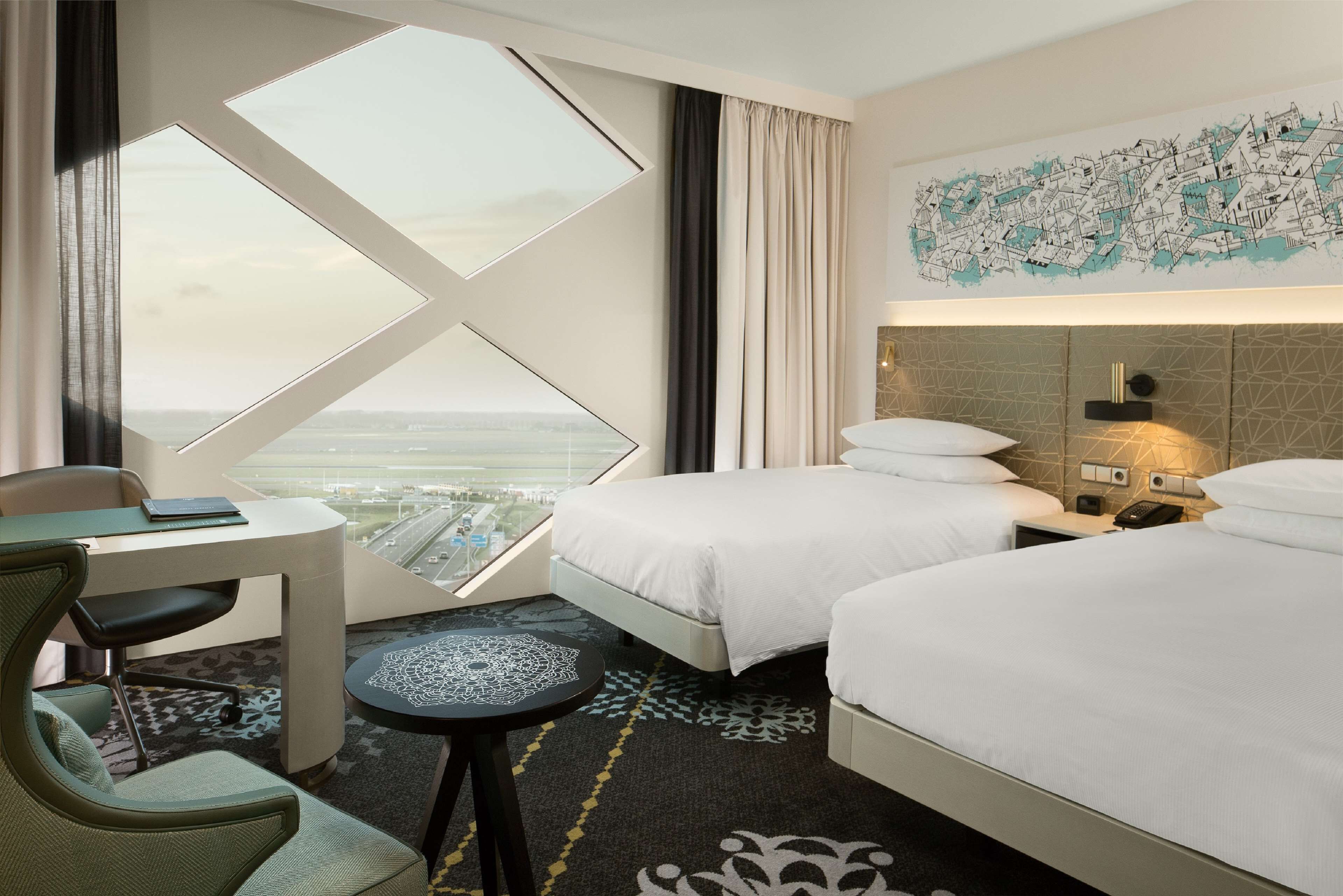 Une chambre d’hôtel avec deux lits, un bureau, une chaise, une vue sur la ville et une grande fenêtre.